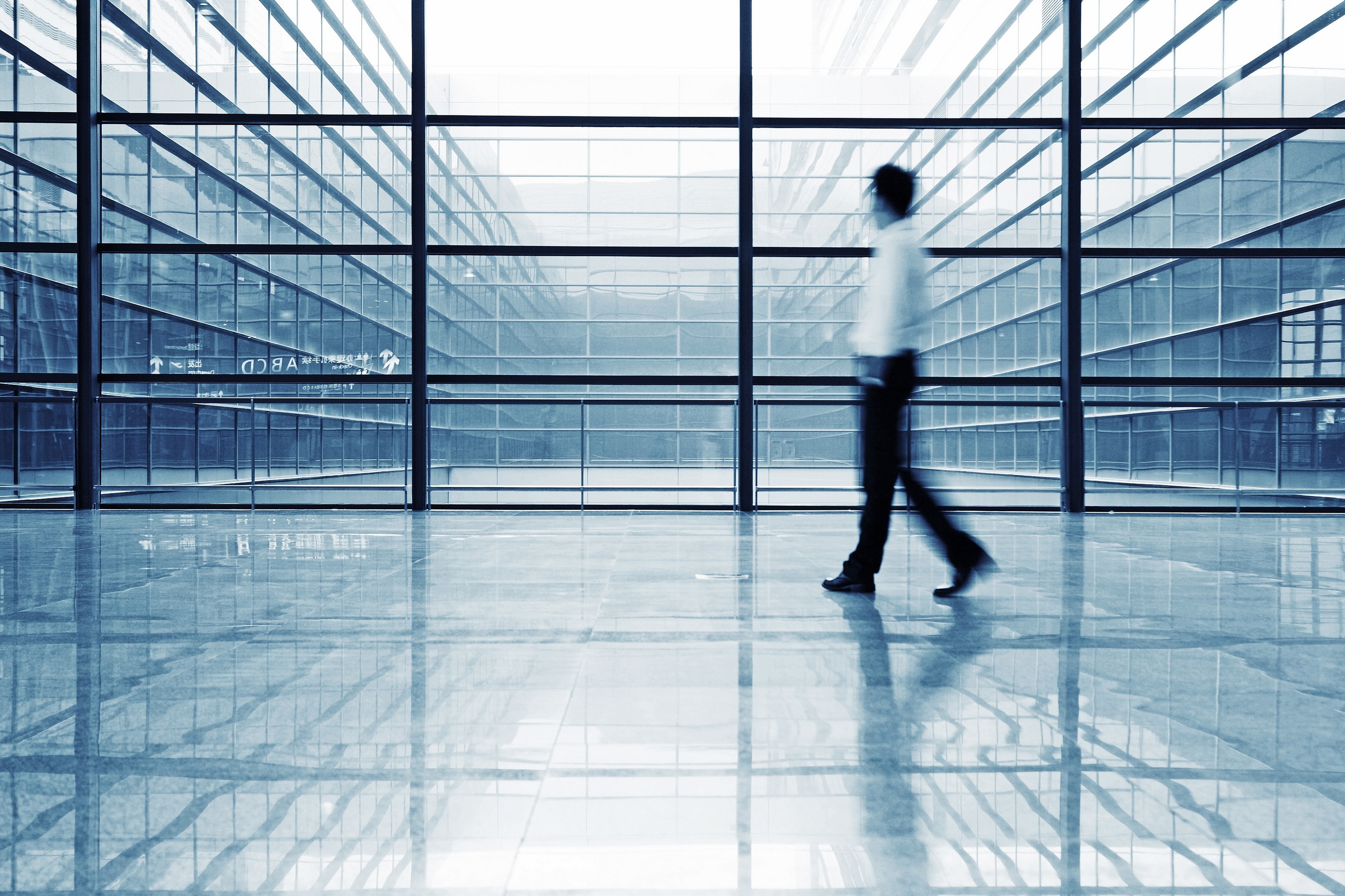 blurred man with white shirt and dark pants walking in office building